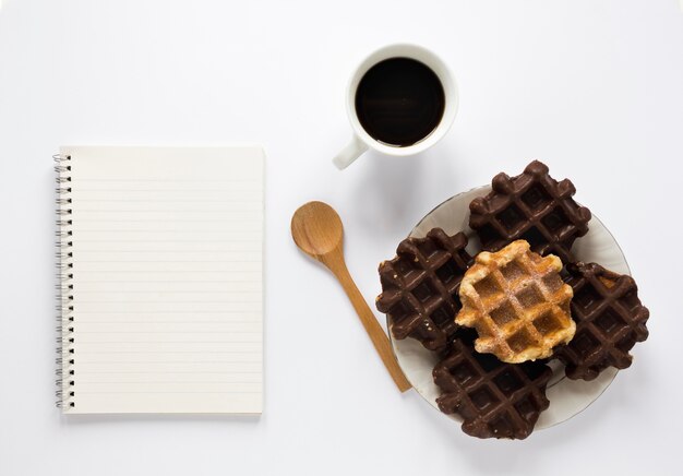 Postura plana de waffles no prato com notebook e café