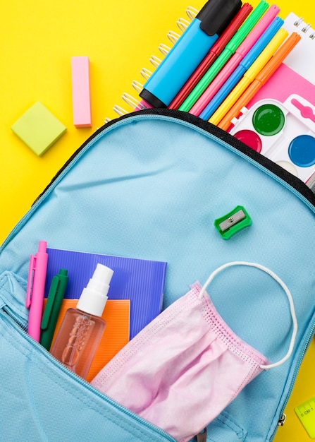 Postura plana dos itens essenciais da escola com mochila e desinfetante para as mãos