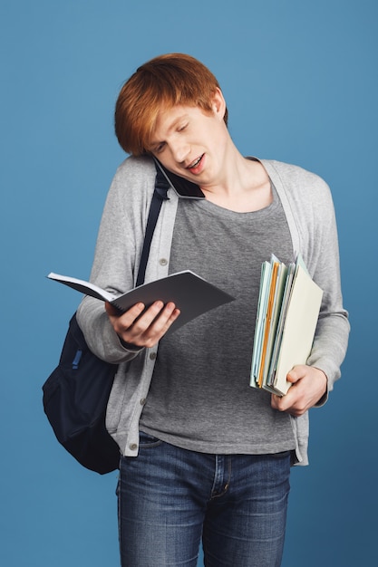 Poucos dias antes do exame. conceito de estudo. jovem estudante ruiva atraente em roupas cinza com mochila preta segurando muitos livros, levando no telefone com um amigo sobre a vida universitária.