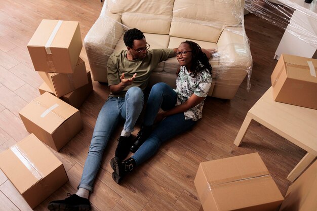 Povos afro-americanos sentados no chão do apartamento depois de se mudarem e se mudarem para uma nova propriedade. Sentindo-se relaxado e feliz por começar novos começos, celebrando o evento da vida. Vista superior de.