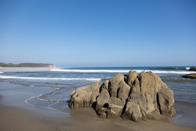 Praia cercada pelo mar e pedras sob o sol e um céu azul no México