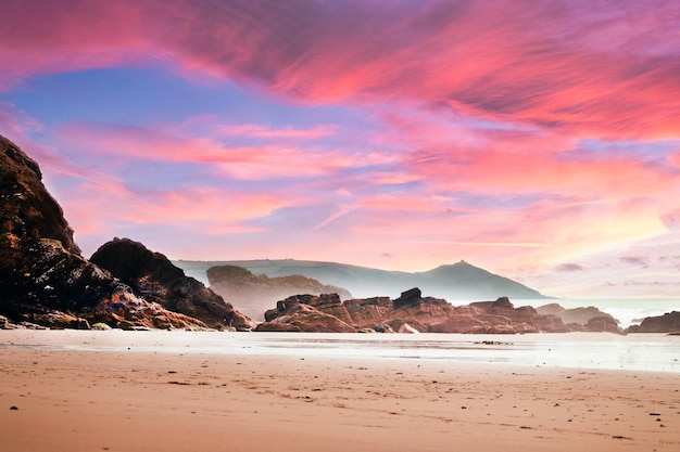 Praia cercada por pedras e mar sob um céu nublado durante um lindo pôr do sol rosa