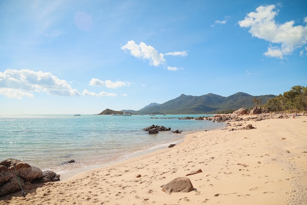 Praia rodeada de rochas e mar com morros cobertos de verde