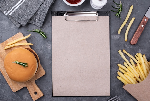 Prancheta ao lado de hambúrguer e batatas fritas