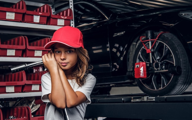 Prateleira com ferramentas, carro brilhante e menina de chapéu com chave grande nas mãos.