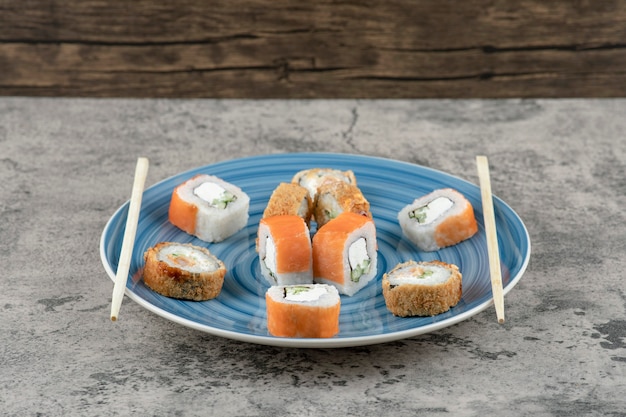 Prato azul de deliciosos rolos de sushi no fundo de mármore