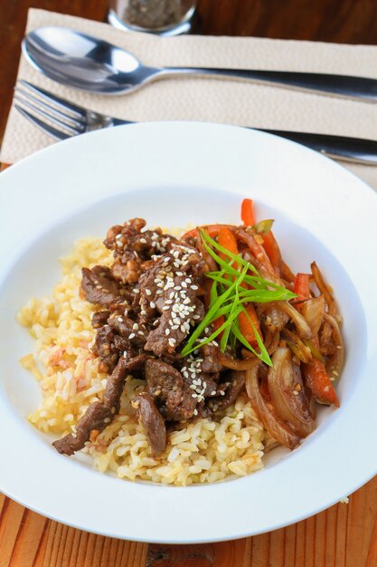 Prato branco de arroz, carne, legumes com temperos e colher e garfo por perto