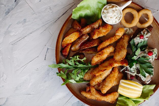 Prato de barro cheio de aperitivos servido com nuggets de frango dourados cozidos com crosta crocante deliciosos canapés com molho de alho de arenque e tomate cereja decorado com salada fresca e queijo