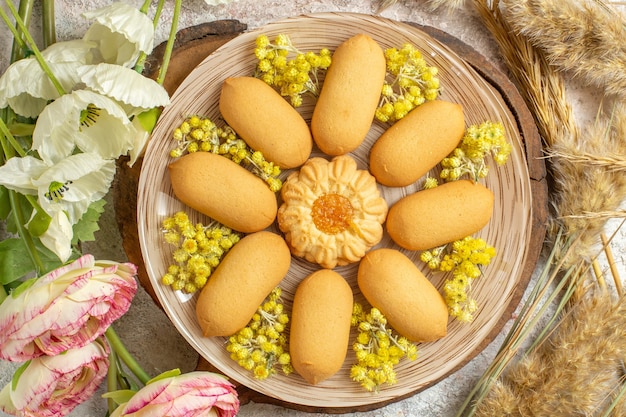 Prato de biscoitos em uma travessa de madeira e flores ao redor em chão de mármore