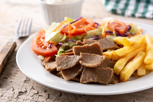 Prato de kebab, legumes e batatas fritas na mesa de madeira