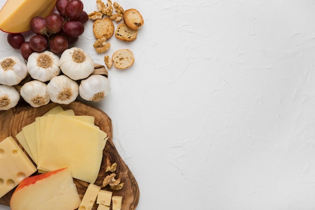 Prato de queijo com bulbo de alho; uvas vermelhas; pão e noz contra fundo de concreto