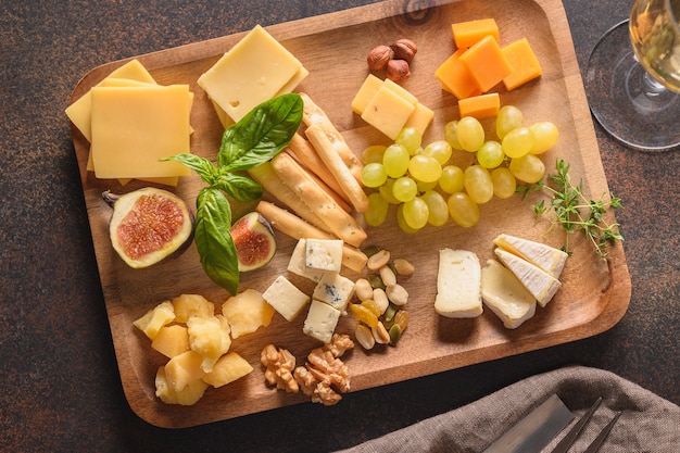 Prato de queijo com uvas, nozes, figos em fundo marrom, vista superior, copie o espaço