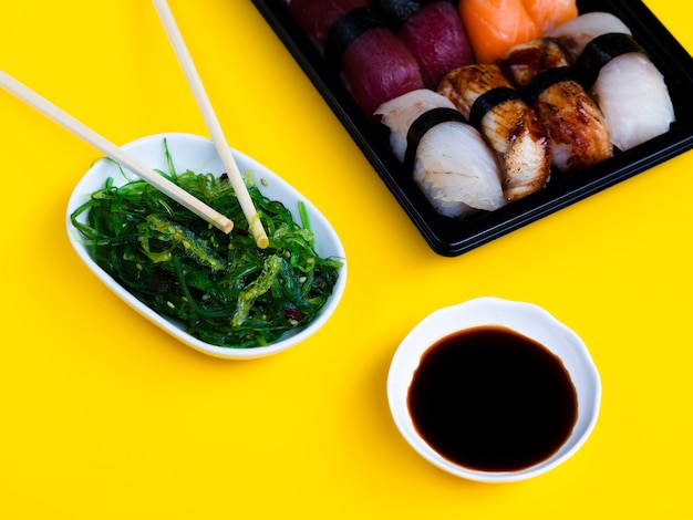 Prato de sushi preto com salada de algas e molho de soja em um fundo amarelo