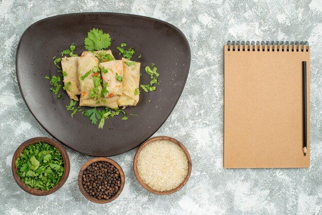 Prato de visão em close-up de prato de comida de repolho recheado e pratos de arroz de papper preto e ervas no lado esquerdo da mesa ao lado do caderno de creme com lápis