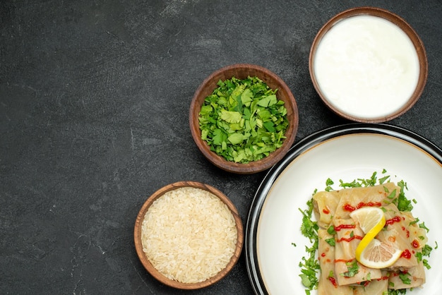 Prato de vista de close-up superior repolho recheado com ervas, limão e molho no prato branco e tigelas com ervas de arroz e creme de leite na mesa preta