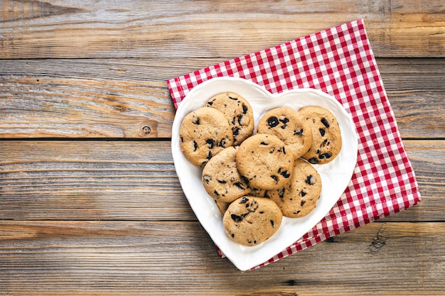Foto grátis prato em forma de coração com biscoitos de chocolate na configuração plana de fundo de madeira