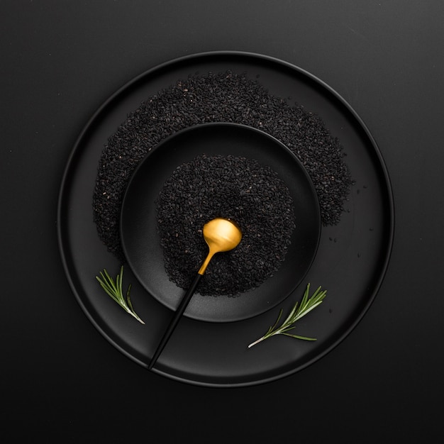 Prato escuro e tigela com sementes de papoila em um fundo preto
