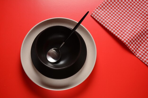 Pratos preto e branco, colher o guardanapo sobre fundo vermelho. arrumando uma mesa