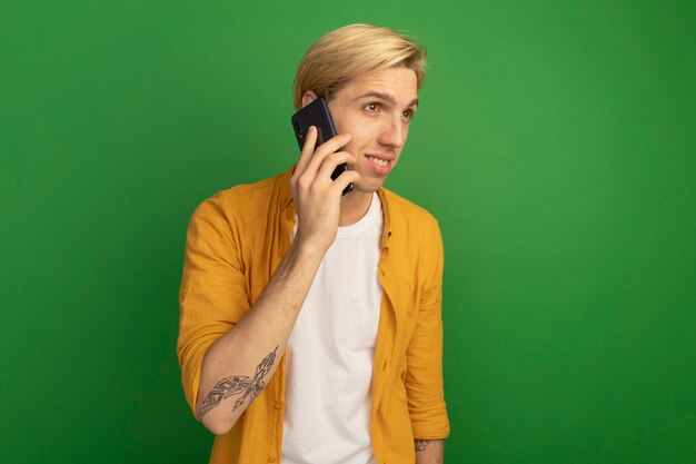 Foto grátis prazer em olhar para o lado jovem loiro de camiseta amarela fala ao telefone isolado no verde com espaço de cópia