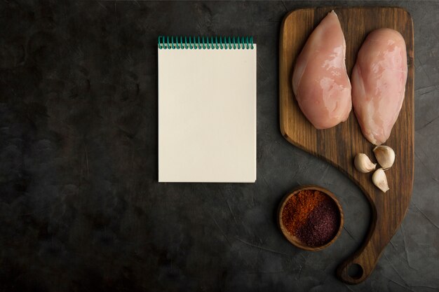 Preparação para cozinhar peito de frango com um livro de receitas à parte