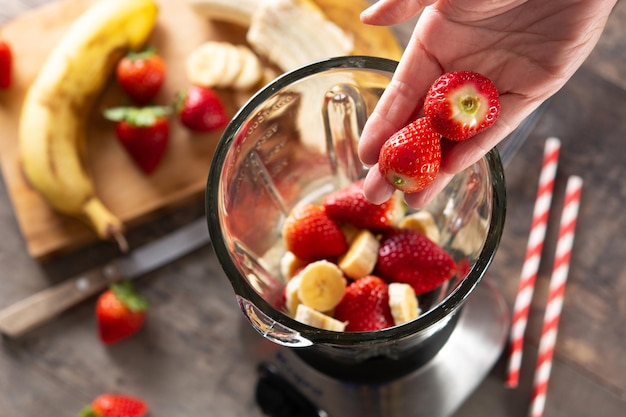 Preparando o smoothie de morango e banana na batedeira na mesa de madeira