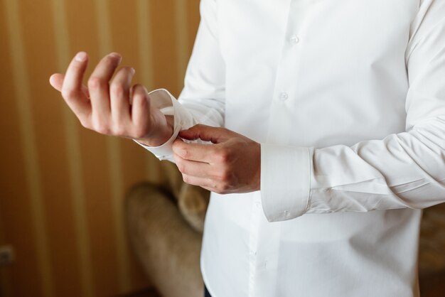 Preparando para o casamento. Noivo abotoando abotoaduras na camisa branca antes do casamento.