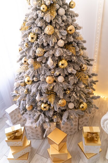 Presentes de natal sob a árvore de ano novo com neve artificial e iluminação dourada Foto Premium