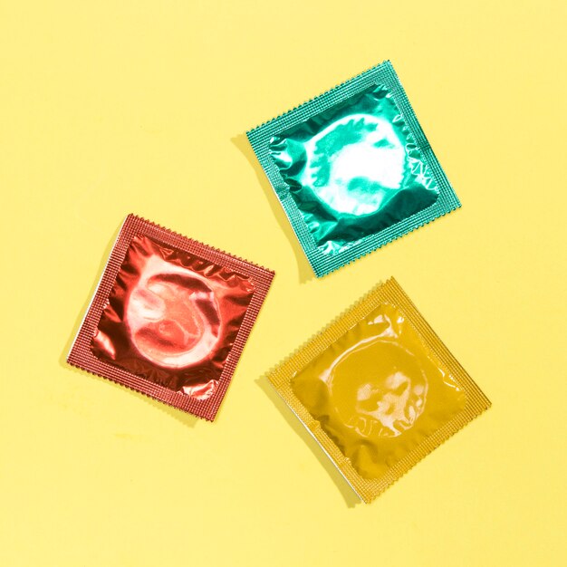Preservativos coloridos da vista superior no fundo amarelo