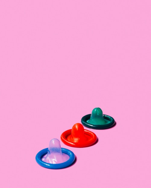 Preservativos coloridos de alto ângulo no fundo rosa