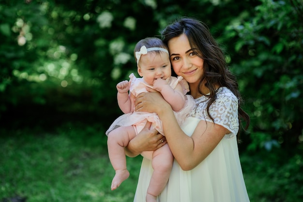 Pretty brunette woman in white dress poses com sua pequena filha no jardim