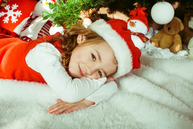 Pretty little girl mentira antes de uma árvore de Natal