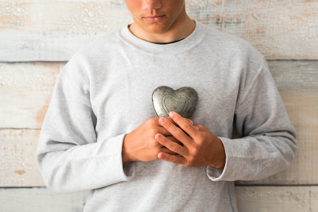 Prevenção e conceito de estilo de vida saudável - homem segurando um coração de metal com uma parede cinza de madeira ao fundo
