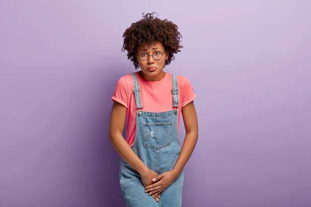Problema médico, conceito de incontáveis. Mulher afro-americana descontente com a barriga para cima, espera perto do banheiro fechado, precisa do banheiro