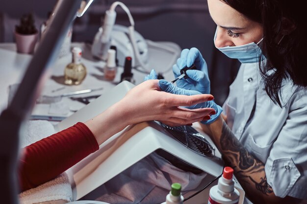 Procedimento de manicure em andamento - mestre esteticista aplicando esmalte colorido. Mãos fechadas