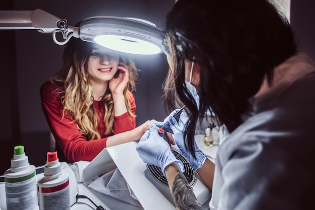 Procedimento de manicure em um salão de beleza - Esteticista fazendo unhas artificiais longas e transparentes para uma cliente do sexo feminino