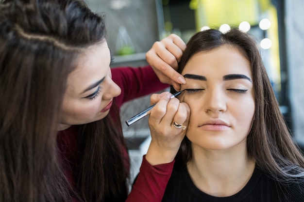 Procedimento de maquiagem das pálpebras para modelo sorridente de cabelos compridos no salão de beleza