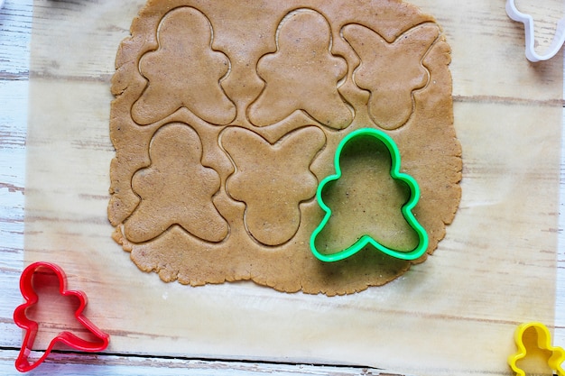 Processo de lidar com biscoitos homem de gengibre, use massa de pão de gengibre de corte de molde de homem de gengibre vermelho no papel manteiga ao redor de cortadores de biscoito coloridos na mesa de madeira branca. vista do topo