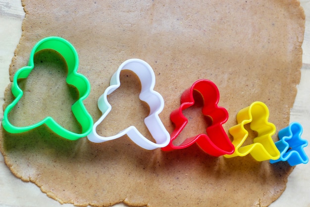 Processo de lidar com biscoitos homem de gengibre, use massa de pão de gengibre de corte de molde de homem de gengibre vermelho no papel manteiga ao redor de cortadores de biscoito coloridos na mesa de madeira branca. vista do topo