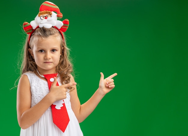 Procurando uma menina usando uma argola de cabelo de natal com pontas de gravata na parte de trás isolada na parede verde com espaço de cópia