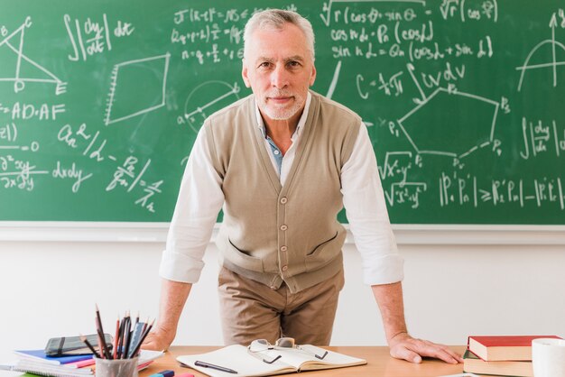 Professor de matemática envelhecido positivo, apoiando-se na mesa