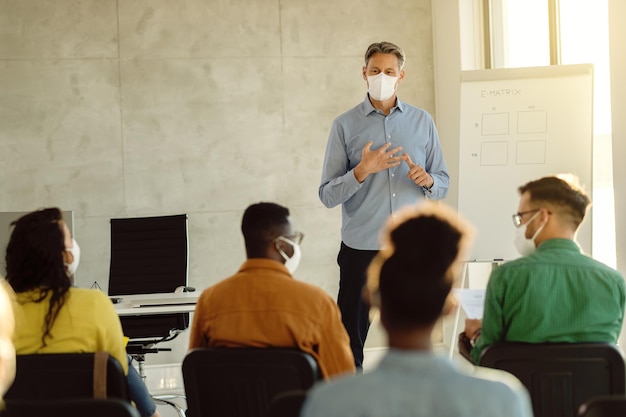 Professor de meia idade com máscaras protetoras conversando com um grupo de estudantes universitários na sala de aula