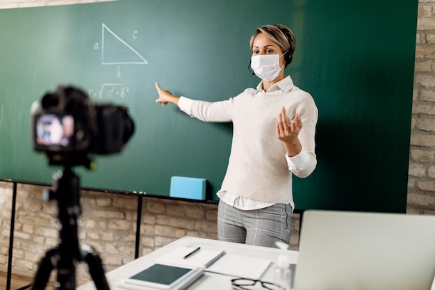 Professor do ensino fundamental apontando para o quadro-negro enquanto ensina matemática online durante a epidemia de coivd-19.