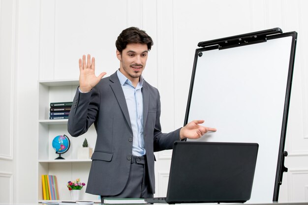 Professor instrutor inteligente de terno cinza em sala de aula com computador e quadro branco dizendo adeus