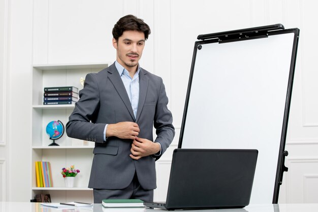 Professor instrutor inteligente em terno cinza em sala de aula com terno de abotoamento de computador e quadro branco