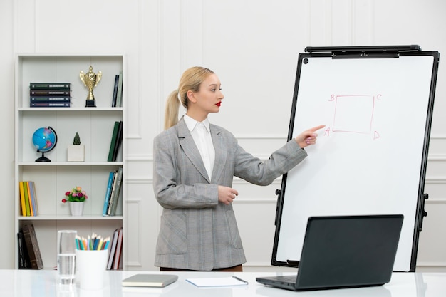 Professor jovem bonito instrutor de terno na sala de aula com laptop e quadro branco apontando para o quadro
