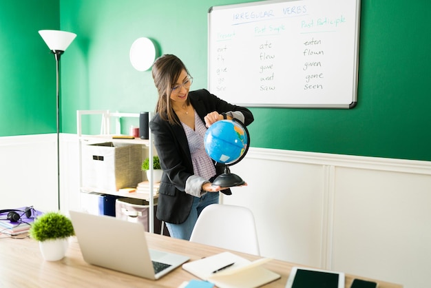 Foto grátis professora atraente ensinando uma aula de geografia enquanto aponta para um país em um globo durante uma videochamada online