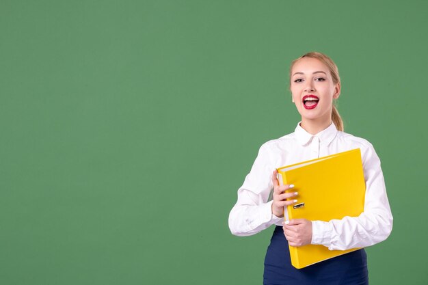 Professora de frente segurando arquivos amarelos em verde