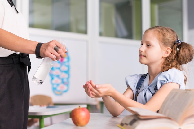 Professora desinfetando as mãos de seu aluno