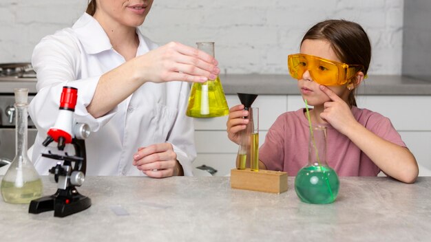 Professora e menina fazendo experiências científicas com tubos de ensaio e microscópio