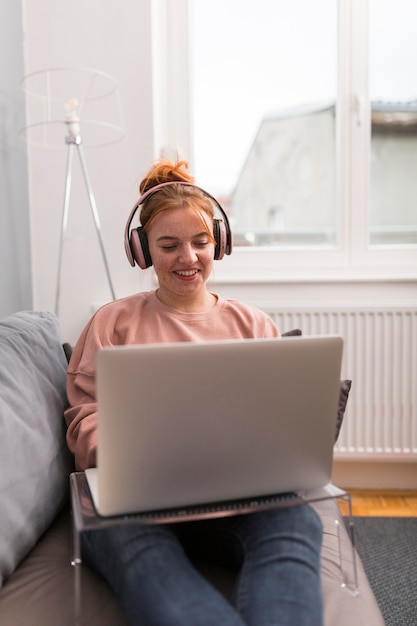 Professora sorridente com fones de ouvido no sofá, segurando uma aula online